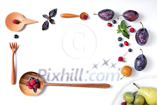 frame of spoons with berries and plums on a white background