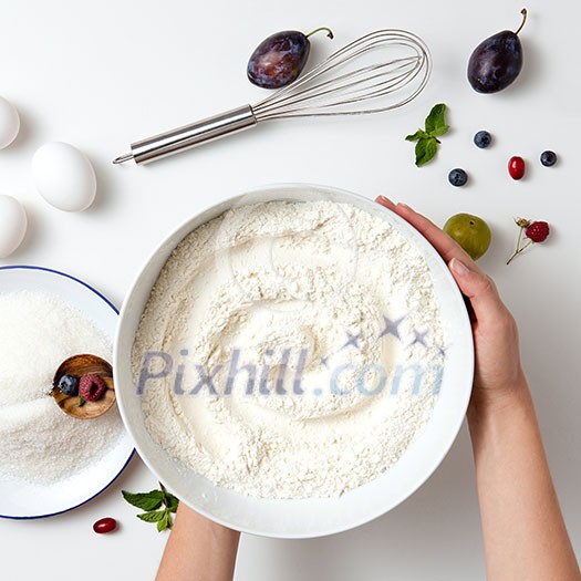 cook hands holding the flour in plate, close ingredients for cake on white table