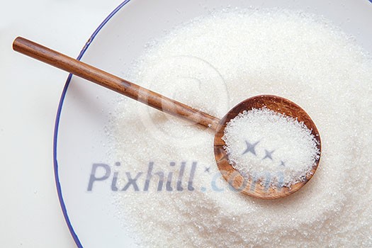 Close-up of granulated sugar in spoon and sugar pile.