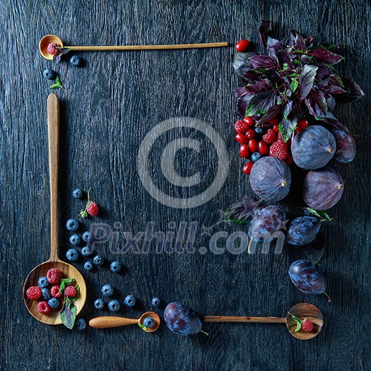 Fresh organic figs, dogwood, blueberries and plums in wooden spoons on wooden background. Frame with copy space.