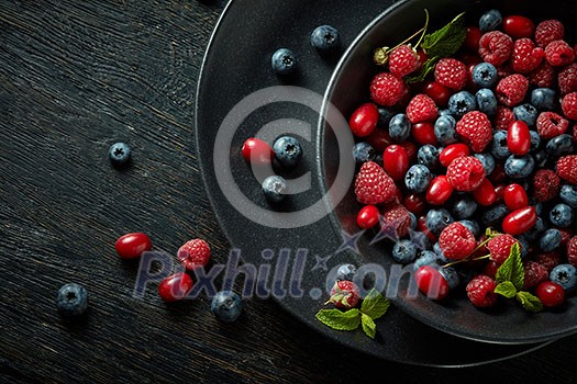 black plate with healthy berries on a black wooden background