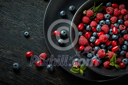 black plate with healthy berries on a black wooden background black plate with healthy berries on a black wooden background