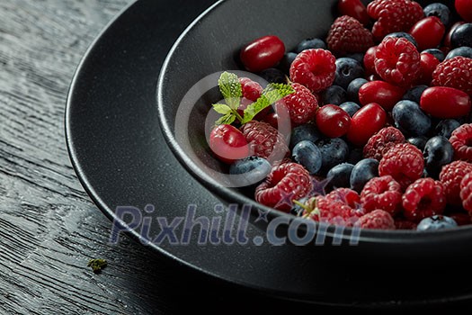 black plate with fresh healthy berries and mint on a dark background