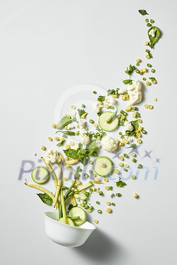 Fresh green vegetarian salad flying out of a bowl isolated on white
