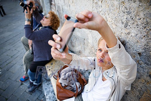 Young female tourist using her smart phone to capture photos from her summer vacation trip in an old italian city she is disovering (shallow DOF; color toned image)
