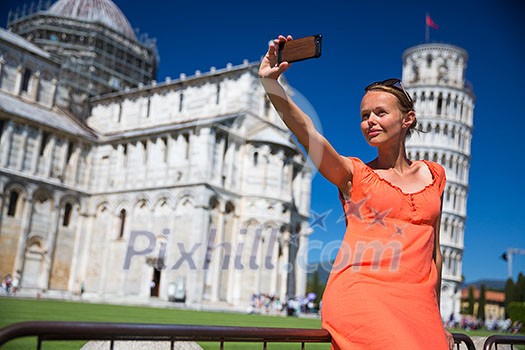 Gorgeous young woman taking a selfie with her smart phone in front of the Leaning Tower of Pisa, Tuscany, Italy (shallow DOF)