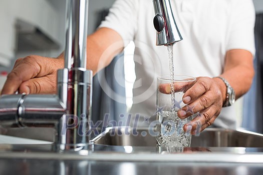 Hands of a senior man pouring a glass of water in a modern kitchen Hands of a senior man pouring a glass of water in a modern kitchen