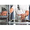 Hands of a senior man pouring a glass of water in a modern kitchen