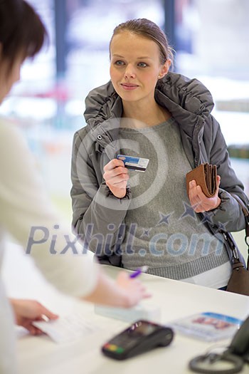 Young woman blowing her nose while in a modern pharmacy, choosing pills to help her with the flu/cold (shallow DOF; color toned image)