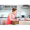 Woman in kitchen with laptop and a glass of wine, browsing the web, shopping online from her modern home (shallow DOF; color toned image)