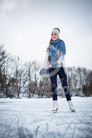 Young woman ice skating outdoors on a pond on a freezing winter day (color toned image; motion blurred image)