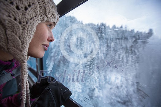 Pretty, young woman admiring splendid winter scenery from a cablecar cabin in high mountains (shallow DOF; color toned image)