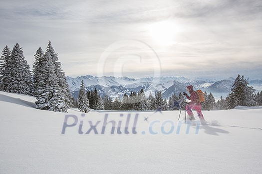 Pretty, young woman snowshoeing in high mountains, enjoying splendid winter weather with abundance of snow