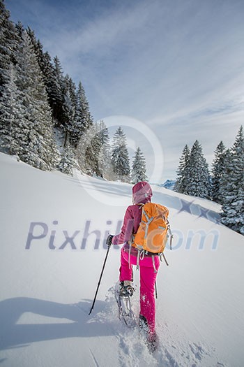 Pretty, young woman snowshoeing in high mountains, enjoying splendid winter weather with abundance of snow