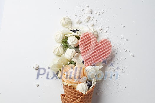 Beautiful flower in ice cream cone with meringues and waffle heart on a white background Beautiful flower in ice cream cone with meringues and waffle heart on a white background