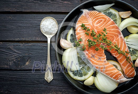 Raw salmon steak with herbs, onion, garlic and salt on a vintage pan on wooden rustic background. Top view. Raw salmon steak with herbs, onion, garlic and salt on a vintage pan on wooden rustic background. Top view.