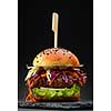 Homemade hamburger with fresh vegetables over black background.