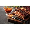 Delicious barbecued ribs seasoned with a spicy basting sauce and served with chopped fresh vegetables on an old rustic wooden chopping board in a country kitchen.