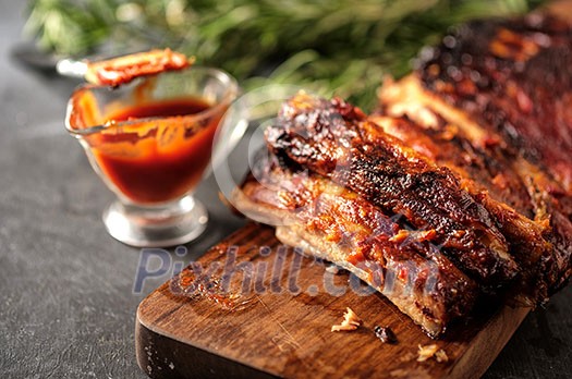 Delicious barbecued ribs seasoned with a spicy basting sauce and served with chopped fresh vegetables on an old rustic wooden chopping board in a country kitchen. Delicious barbecued ribs seasoned with a spicy basting sauce and served with chopped fresh vegetables on an old rustic wooden chopping board in a country kitchen.