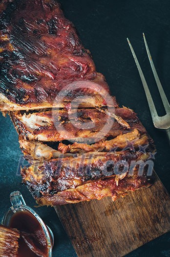 Delicious barbecued ribs seasoned with a spicy basting sauce on an old rustic wooden chopping board in a country kitchen. Top view. Retro toned. Delicious barbecued ribs seasoned with a spicy basting sauce on an old rustic wooden chopping board in a country kitchen. Top view. Retro toned.