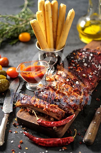 Delicious barbecued ribs seasoned with a spicy basting sauce and served with chopped fresh vegetables on an old rustic wooden chopping board in a country kitchen. Delicious barbecued ribs seasoned with a spicy basting sauce and served with chopped fresh vegetables on an old rustic wooden chopping board in a country kitchen.