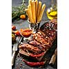 Delicious barbecued ribs seasoned with a spicy basting sauce and served with chopped fresh vegetables on an old rustic wooden chopping board in a country kitchen.