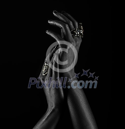 Dark-skinned hand with jewelry on a black background. Hands close up of young woman with black manicure with rings. Luxury lifestyle.