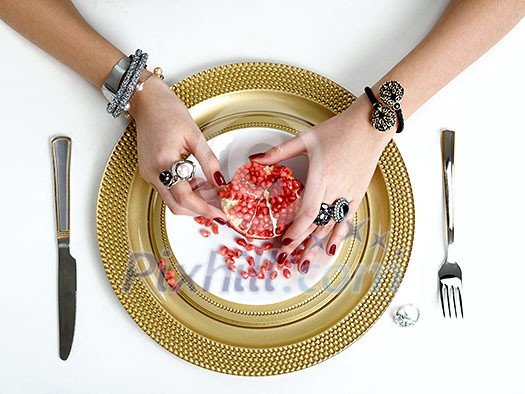 Beautiful female hands with jewelry at the table with a pomegranate on a plate. Beautiful female hands with jewelry at the table with a pomegranate on a plate.