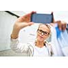 Pretty, female tourist taking a selfie picture while visiting a foreign city and its highlights landmarks, looking happy and relaxed. loving the travel (shallow DOF; color toned image)