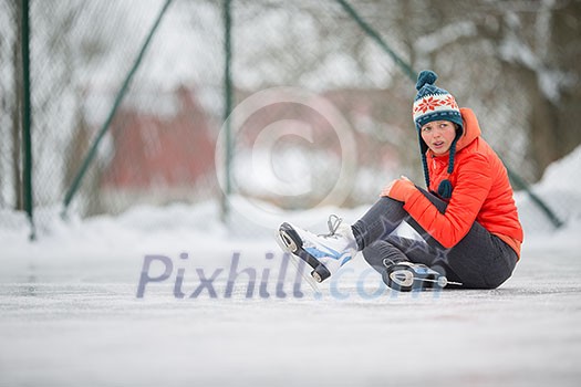 Ice skating concept - young woman sitting on the ice rink after falling down and hurting her knee