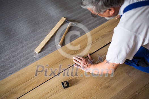 DIY, repair, building and home concept - close up of male hands lying parquet floor board/laminate flooring (shallow DOF; color toned image)