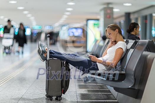 Young female passenger at the airport, using her tablet computer while waiting for her flight (color toned image)