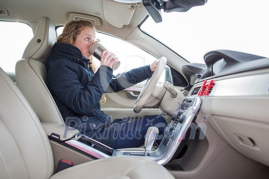Woman driving a car - female driver at a wheel of a modern car, drinking her morning coffee (shallow DOF; color toned image) Woman driving a car - female driver at a wheel of a modern car, drinking her morning coffee (shallow DOF; color toned image)
