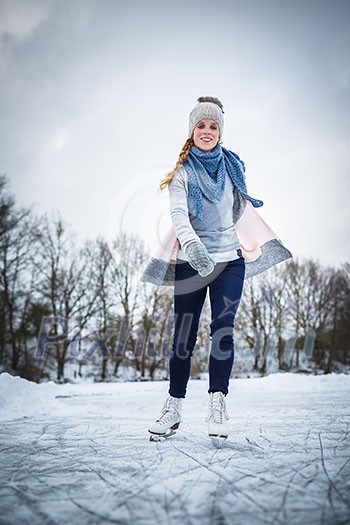 Young woman ice skating outdoors on a pond on a freezing winter day (color toned image; motion blurred image)