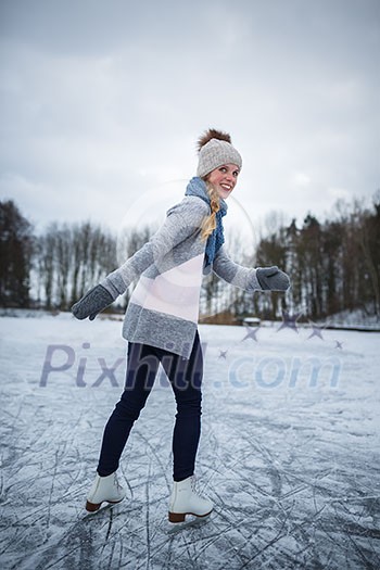 Young woman ice skating outdoors on a pond on a freezing winter day (color toned image; motion blurred image)