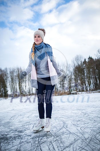 Young woman ice skating outdoors on a pond on a freezing winter day (color toned image; motion blurred image)