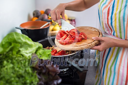 Young woman cutting vegetables in her modern kitchen - fixing a salad