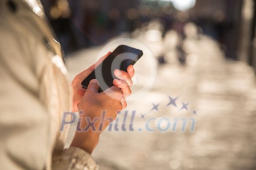 Young woman messaging/using an app on her smart-phone in a city street context (shallow DOF; color toned image)