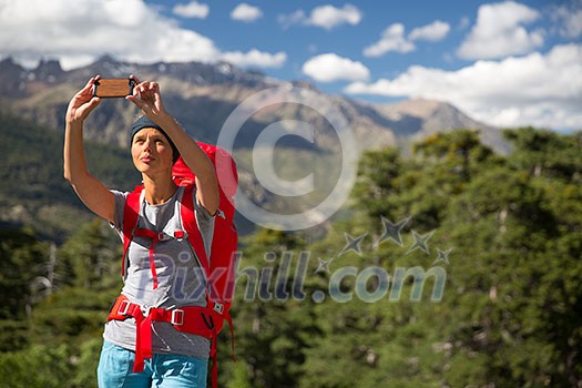 Pretty, young woman hiker taking a selfie photo with her smart phone in high mountains