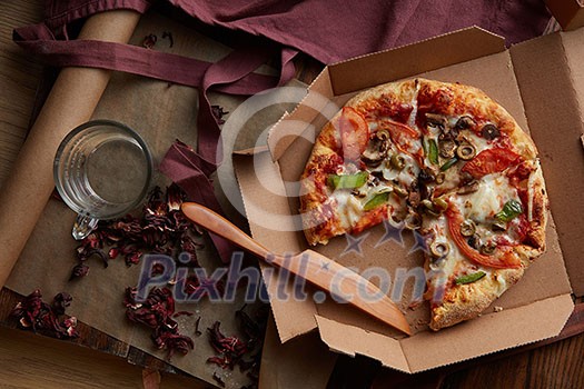 Pizza concept. Delicious pizza represented on kitchen table. Fresh pizza in cardboard box on wooden table top view. Glass of water top view.
