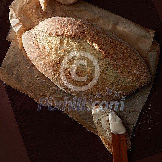 Loaf of bread over cooking paper over wooden background. Delicious white bread for having breakfast, dinner, lunch, etc.