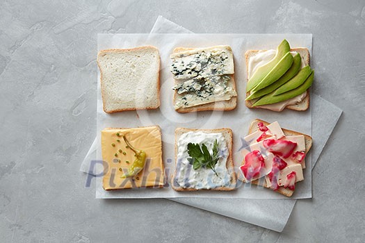 Variety of vegetarian toast sandwiches with cheese, avocado, cabbage and pepper on parchment paper on a gray concrete background