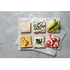 Variety of vegetarian toast sandwiches with cheese, avocado, cabbage and pepper on parchment paper on a gray concrete background
