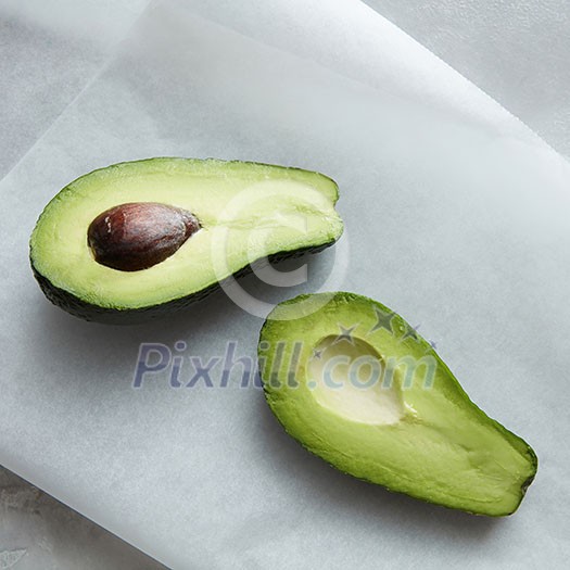 Fruit avocado represented on white baking paper over table. Green colored avocado with brown bone. Fruit avocado represented on white baking paper over table. Green colored avocado with brown bone.