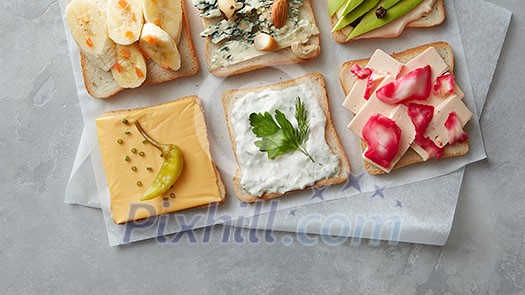 Different kinds of colorful sandwiches on white chalkboard background from above (top view). Party starter or appetizer - flat lay composition.