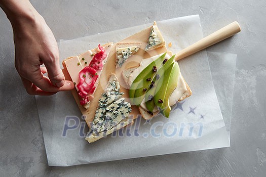Human hand takes a sandwich with cheese and vegetables from a wooden board on a concrete background