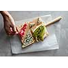 Human hand takes a sandwich with cheese and vegetables from a wooden board on a concrete background