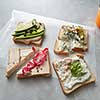 Slices of sandwiches with cheese and vegetables on parchment on a concrete background