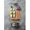 Open pan and sliced vegetables for cooking with baguette on a gray concrete background, flat lay