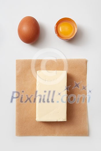Top view of butter block on paper with raw chicken eggs over white background Top view of butter block on paper with raw chicken eggs over white background